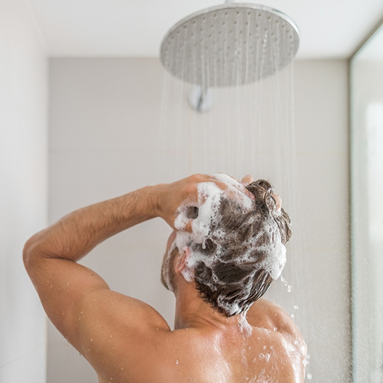 Man wast zijn haren met schuimende shampoo onder de douche