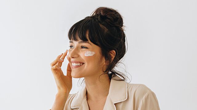 Vrouw met donkere haren brengt dag- of nachtcrème aan tijdens haar skincare routine. Vrouw met donkere haren brengt dag- of nachtcrème aan tijdens haar skincare routine.