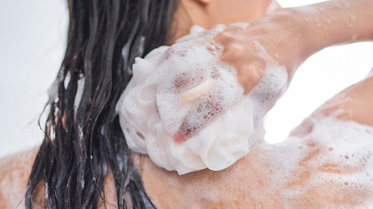 Vrouw die zich inschuimd met douchegel onder de douche en lacht. Vrouw die zich inschuimd met douchegel onder de douche en lacht.