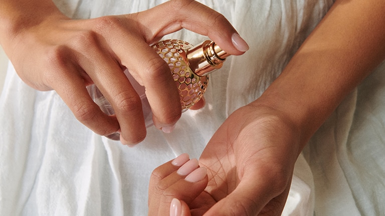 Vrouw in witte jurk die parfum op haar pols sprayed Vrouw in witte jurk die parfum op haar pols sprayed