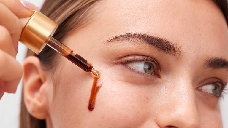 Ingezoomd vrouwengezicht die tanning drops aanbrengt met een pipet. Ingezoomd vrouwengezicht die tanning drops aanbrengt met een pipet.