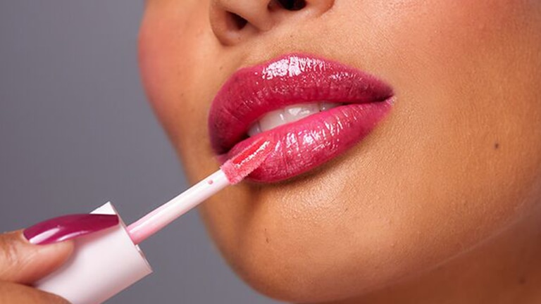 Ingezoomd vrouwen gezicht die roze lipgloss aanbrengt met een lipgloss borsteltje. Ingezoomd vrouwen gezicht die roze lipgloss aanbrengt met een lipgloss borsteltje.